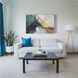 A living room with a white sofa and a canvas print featuring a geometric abstract design with intersecting lines and teal, green, beige, gray, and gold tones.