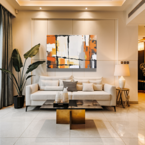 Canvas art featuring a geometric design with orange, black, and white hues, displayed above a cream-colored sofa in a modern living room.